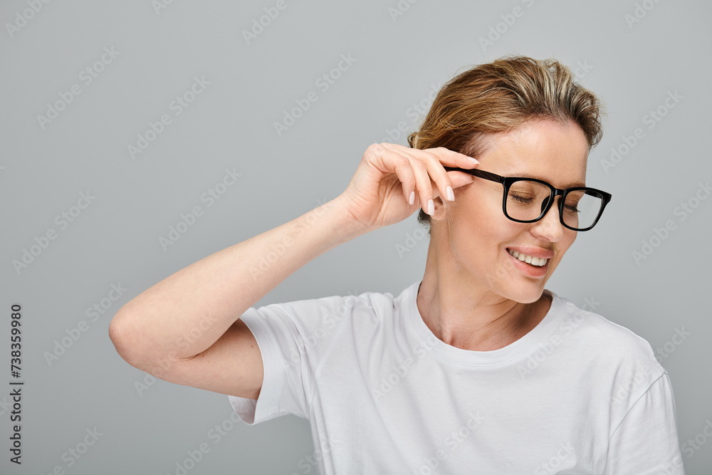 joyous appealing woman with blonde hair and stylish glasses posing on gray backdrop and looking away
