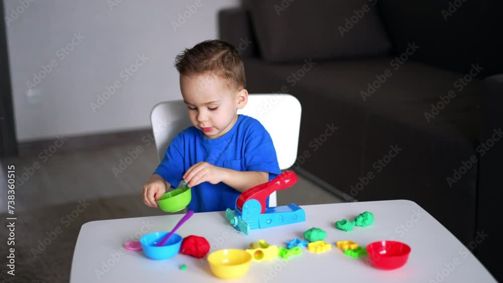 Sweet baby boy sitting at desk plays with plasticine. Toddler takes a piece of plasticine and a stick to cut it. Sweet baby boy sitting at desk plays with plasticine. Toddler takes a piece of plasticine and a stick to cut it.