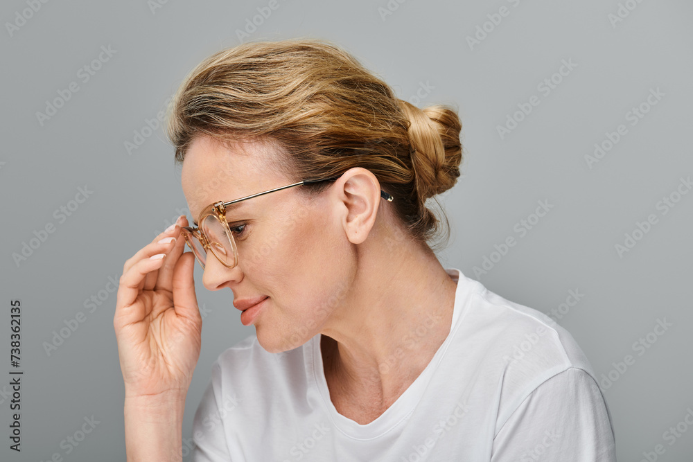 appealing jolly woman with blonde hair and glasses in casual attire looking away on gray backdrop