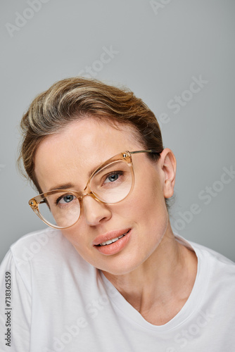 happy good looking woman with blonde hair and glasses smiling at camera on gray background