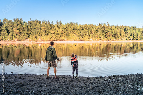 Father and son spending time outdoors enjoying nature in beautiful forest lake setting having fun throwing rocks 