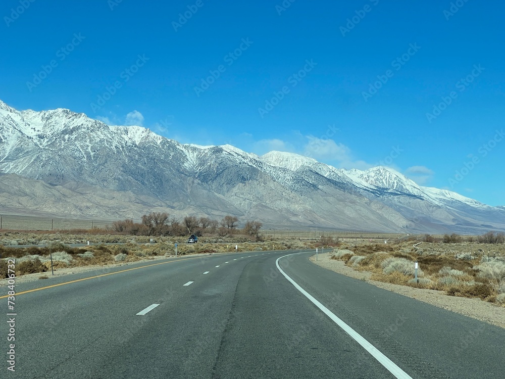 Freeway curves with dramatic view of snow capped mountains. Desert landscape in foreground, alongside US Route 395, near Independence, California