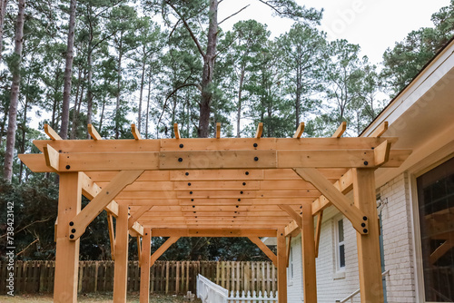 The rear back exterior of a newly painted and renovated white brick ranch style house with a large yard and a newly built wood arbor pergola for shade photo