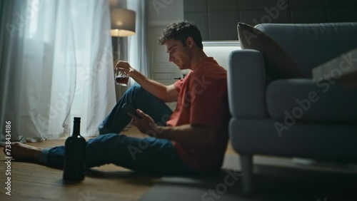 Lonely alcoholic drinking whiskey glass alone in room. Breakup man waiting sms photo