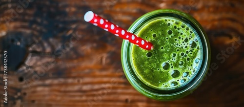 Green detox smoothie in a glass jar, with a red straw decorated with white dots, on a wooden surface.
