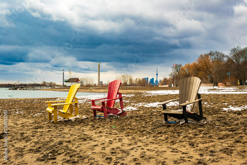 Bright yellow and red beach chairs on a sandy beach in winter with dramatic clouds and downtown city skyline in background room for text Kew beach Toronto beaches neighbourhood