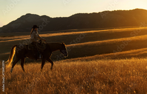 Wyoming Cowgirl at sunrise rolling hill golden glow riding horse
