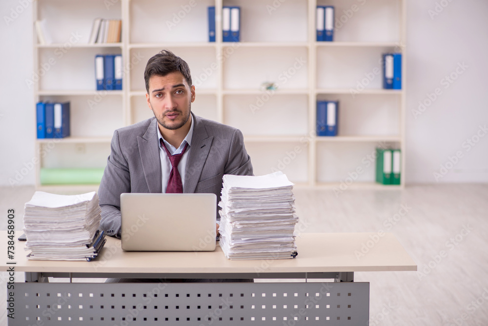 Young male employee unhappy with excessive work in the office Young male employee unhappy with excessive work in the office