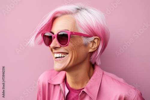 Portrait of a happy young woman with pink hair and sunglasses over pink background © Igor