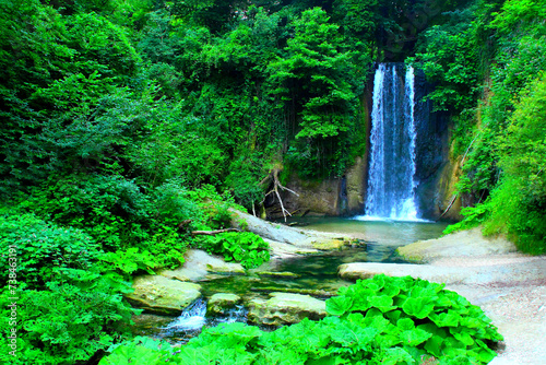 Short-exposure capture of Cascata dell Antico Mulino in Sarnano  an enchanting place with plenty of green plants  trees and the waterfall s abundant waters flowing from above and splashing down below