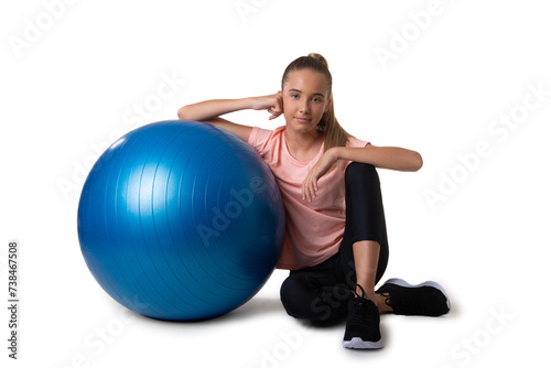 attractive and fit teen girl sitting on floor close to a swiss blue ball, isolated on white background