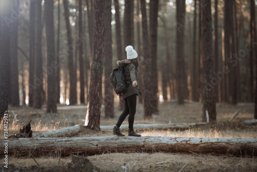 Woman balancing on fallen tree in Gnangara pine plantation, Perth Western Australia wearing backpack, green jacket and white beanie. Concept of exploration, fun, outdoor adventure