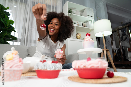 Beautiful young African blogger presenting piece of cupcake in concept showing special cuisine in pastel color. Content creating of social media with favorite sweets bakery dish. Tastemaker. photo