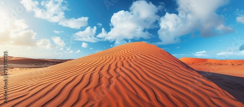 Close-up of a stunning red sand dune with wind patterns against a blue sky.