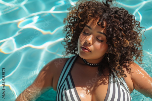 A beautiful young latin American woman plus size in a striped swimsuit in the pool. body positive, enjoying the moment.