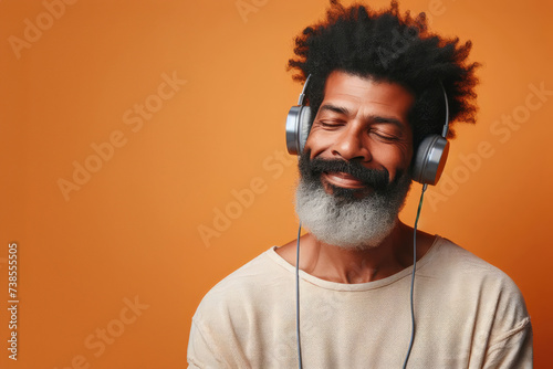 An African American middle aged man with a beard wearing headphones happy enjoying an audition, on an orange background in casual clothes photo