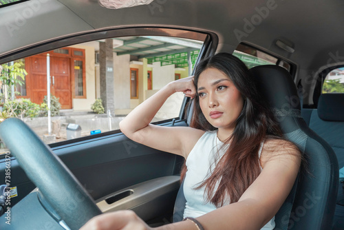 Tired female driver sits at wheel, has empty expression as daydreaming to drive car by herself.