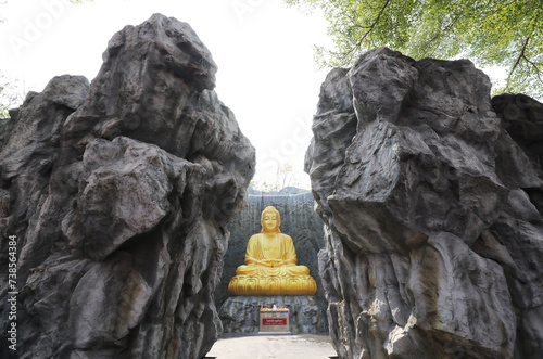 The big golden Buddha statue with waterfall and stone wall in background at Wat Lak Si Rat Samoson, Samut Sakhon, Thailand. photo