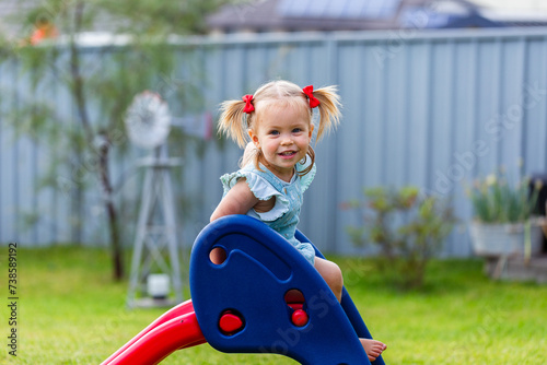 Toddler girl climbing on plastic slide equipment in backyard on overcast day photo