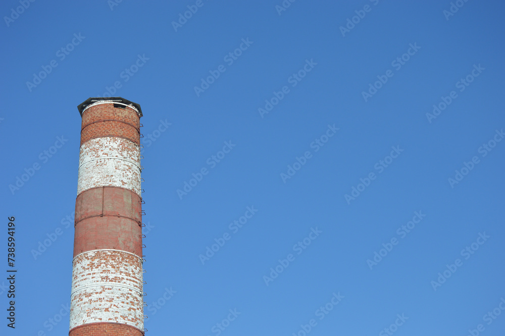 Red and white round brick chimney of a boiler room against a blue sky.
