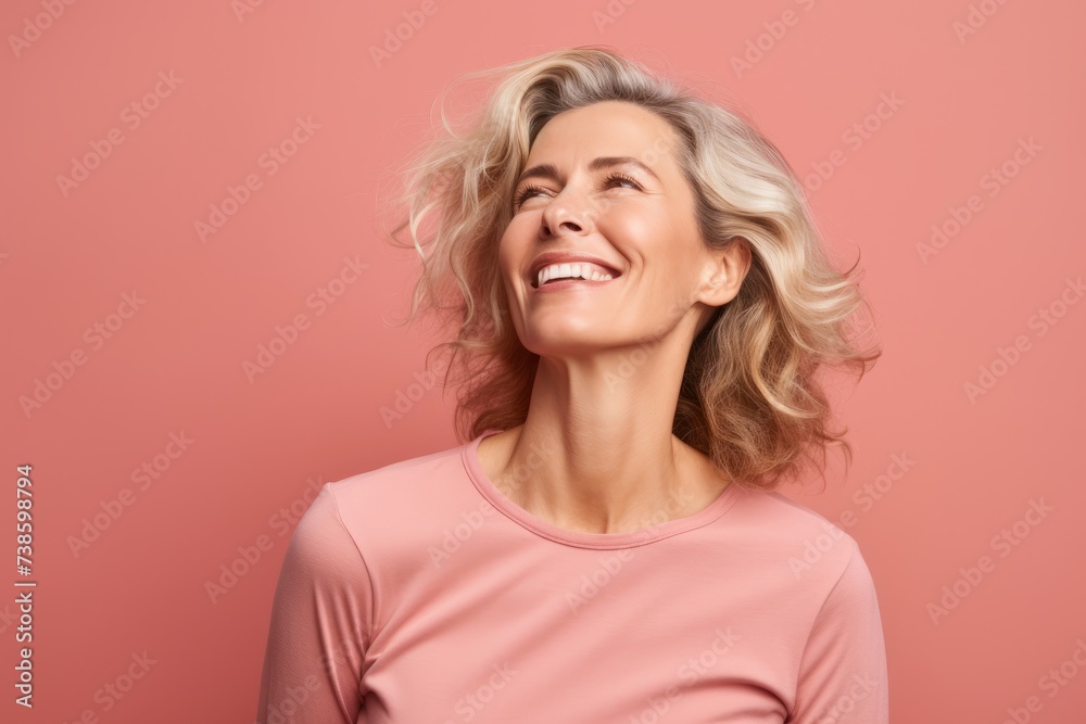 Cheerful young woman looking up and smiling while standing against pink background Cheerful young woman looking up and smiling while standing against pink background