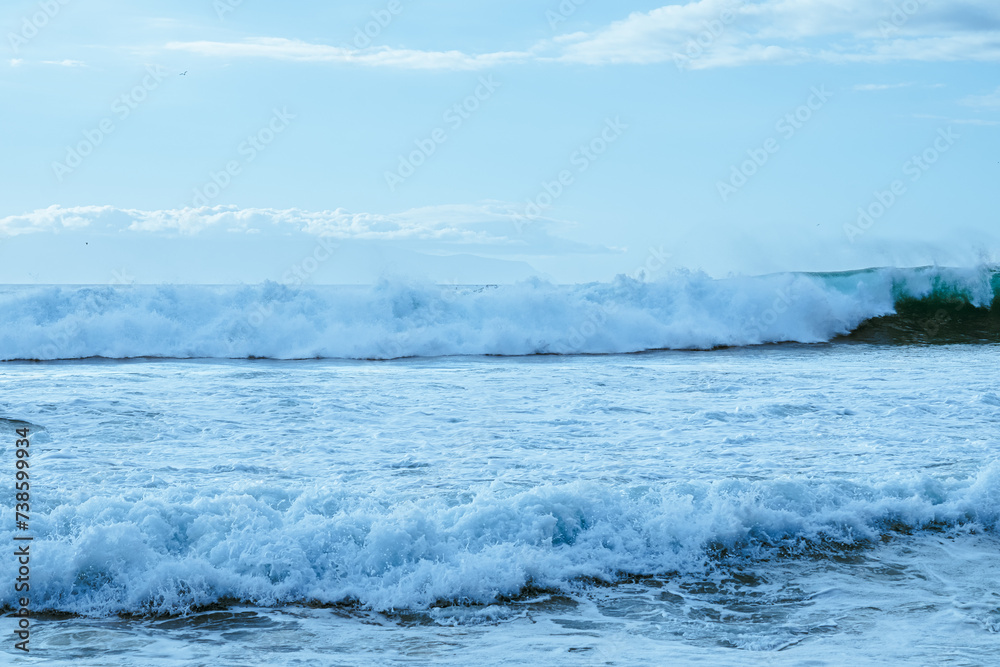 Panoramic sea view from the beach with splashing waves. Blue sky and horizon over ocean water in the background with the outline of an island