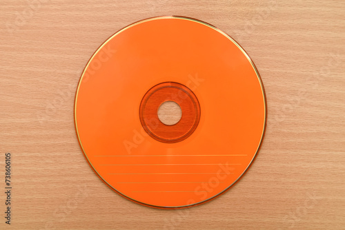 Orange CD or DVD on the brown wooden table. Vintage technology concept. Top view.