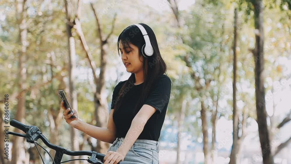 Lifestyle, education, adolescence. Teenage student in headphones with smartphone bicycle sitting in park, female looks at phone screen Lifestyle, education, adolescence. Teenage student in headphones with smartphone bicycle sitting in park, female looks at phone screen