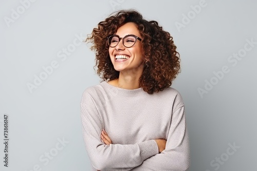 Portrait of a smiling young woman with curly hair and eyeglasses against grey background