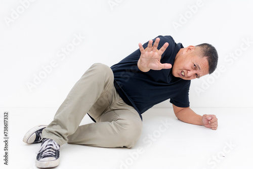 A scared middle aged Asian man drops on the ground showing fear with a defensive posture, begging not to be harmed.