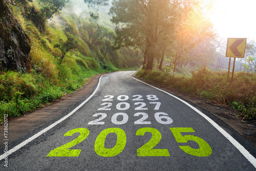 The year 2025-2028 is written on the highway in the middle of an empty asphalt road and a beautiful forest with the sun shining. The concept of goals, vision and business objectives 2025-2028.