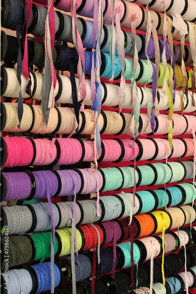 Fototapeta premium Bobbins with various colorful ribbons on counter in store. Needlework and sewing supplies. Colorful ribbon on rack in craft shop. Artisan and handicraft material. DIY hobby concept