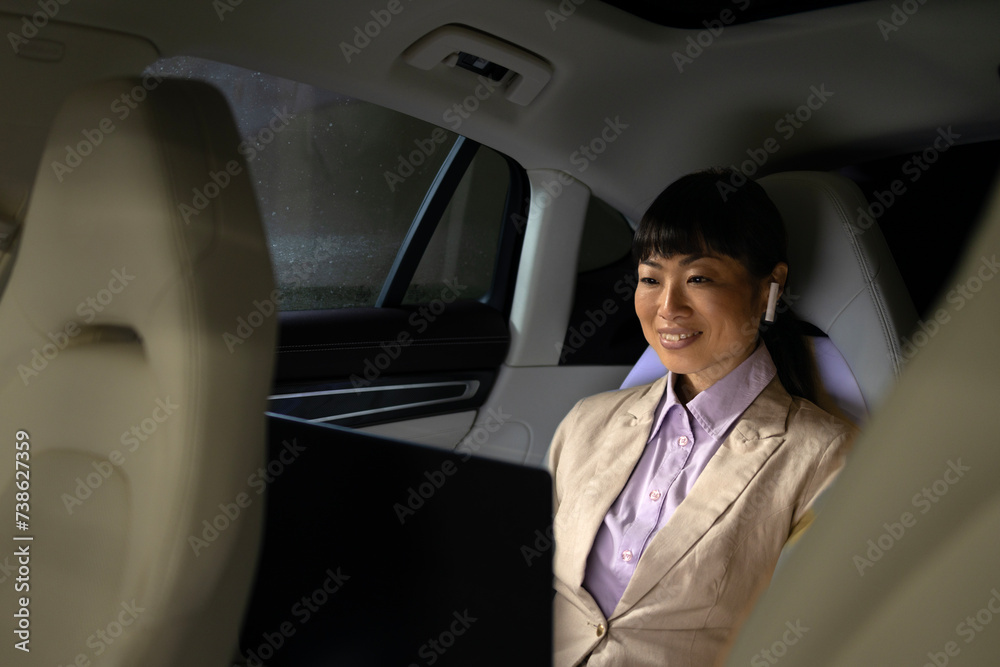 Businesswoman enjoying comfortable ride in luxurious limousine while working on laptop computer.