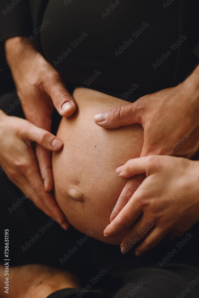Close up photo of pregnant woman and her husband holding pregnant belly at home.