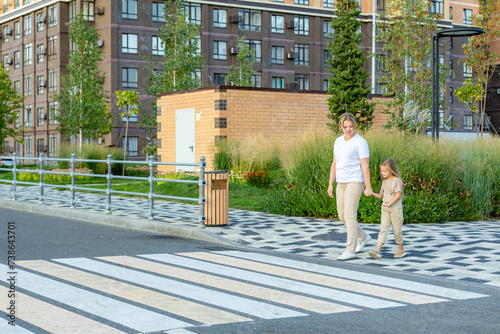 Bilde på lerret Young mother holds hand of little daughter and crossing road in modern urban district, residential neighborhood