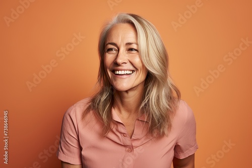 Portrait of smiling senior woman looking at camera over orange background. © Loli
