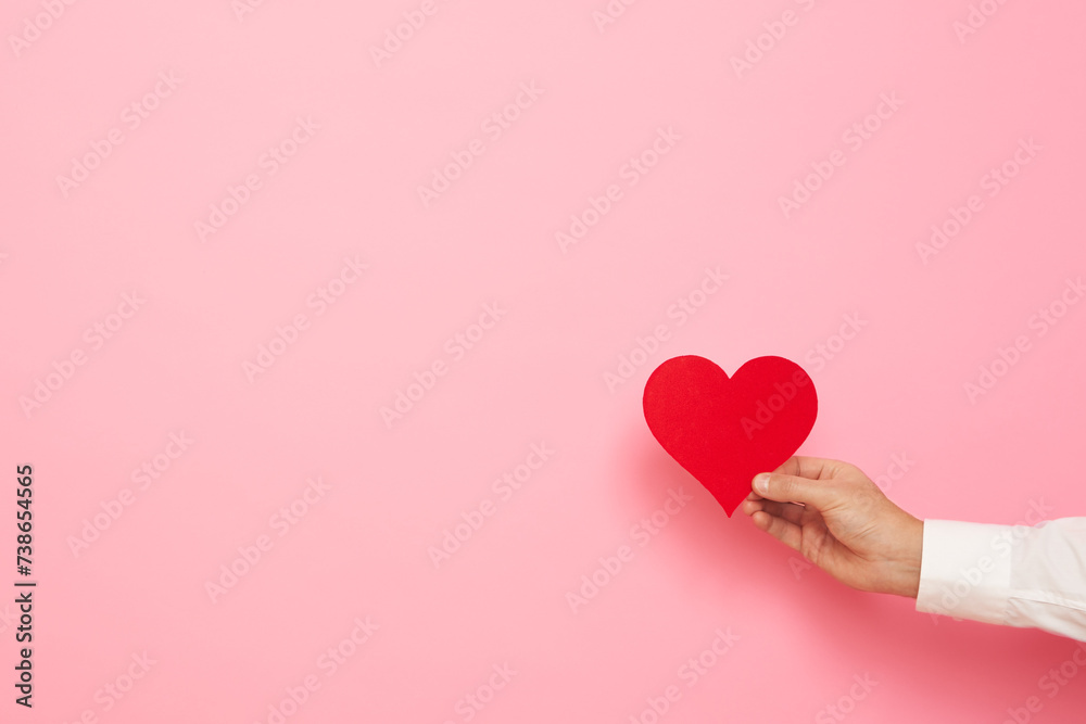 Man hand with paper heart figure on pink background. International Women's Day celebration Man hand with paper heart figure on pink background. International Women's Day celebration