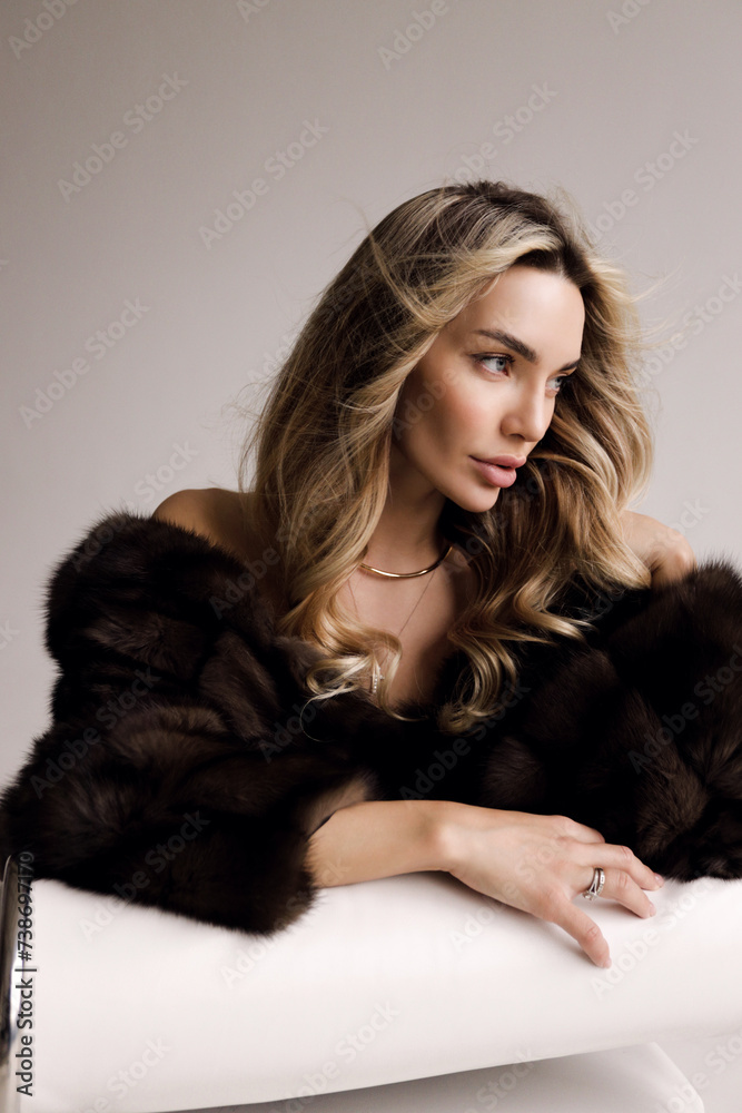 beautiful sexy woman with blond hair in luxurious fur coat posing in the studio