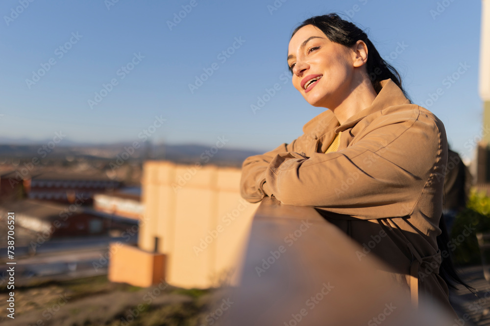 smiling woman leaning on railing looking at the horizon at sunset