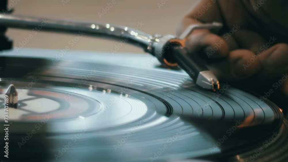Close-up of a hand which changing song on a vinyl record by moving the turntable needle on a vintage record player. Concept of warm indoor atmosphere of enjoying music