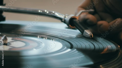 Close-up of a hand which changing song on a vinyl record by moving the turntable needle on a vintage record player. Concept of warm indoor atmosphere of enjoying music photo