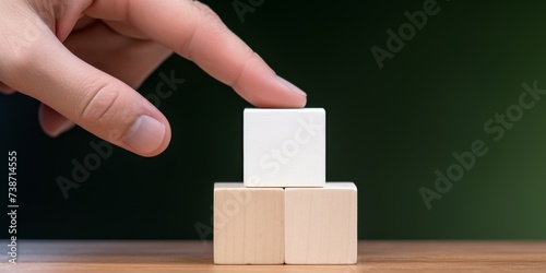 The index finger of the hand touches a wooden cube, which stands on two other cubes, on a dark background, with free space