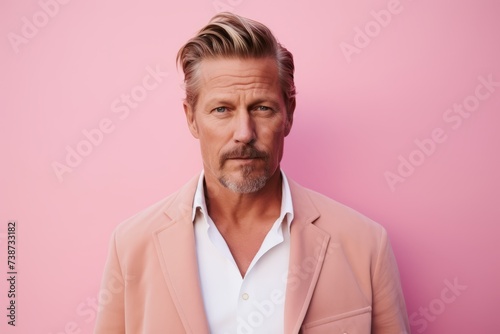 Serious mature man looking at camera with serious expression, standing against pink background