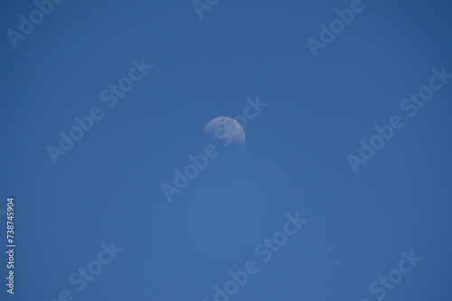 A view of the moon with blue sky in the daytime. 