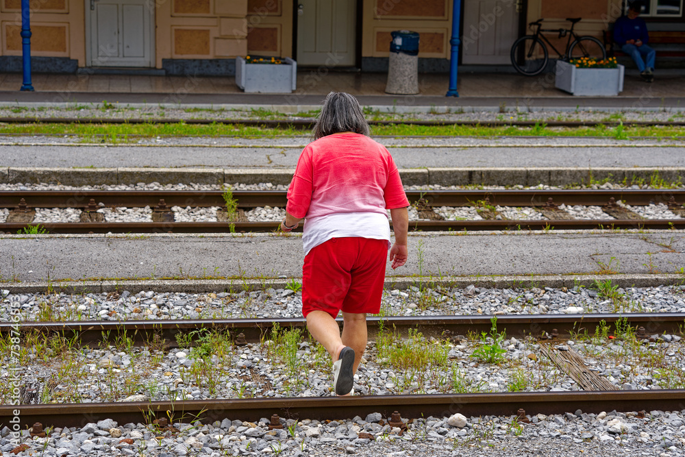 Middle aged woman crossing railway tracks at train station of Slovenian City of Kranj on a cloudy summer day. Photo taken August 9th, 2023, Kranj, Slovenia. Middle aged woman crossing railway tracks at train station of Slovenian City of Kranj on a cloudy summer day. Photo taken August 9th, 2023, Kranj, Slovenia.