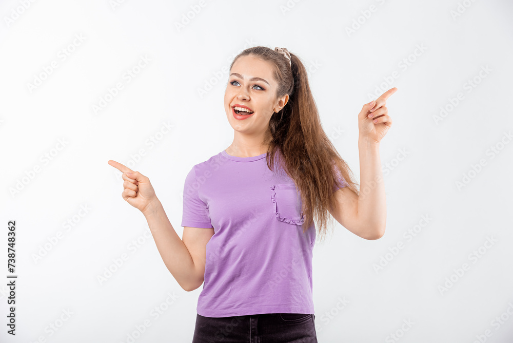 Enthusiastic young woman with long hair, pointing fingers in different directions with happy face and smiling, makes a choose, wearing purple t-shirt, white background Enthusiastic young woman with long hair, pointing fingers in different directions with happy face and smiling, makes a choose, wearing purple t-shirt, white background