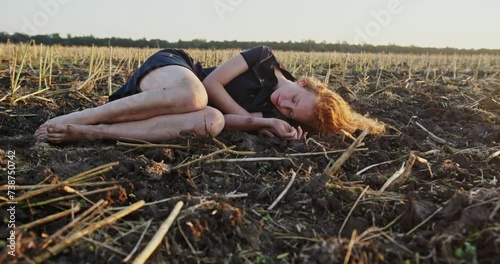 Depressed young woman lying on ground with dry grass