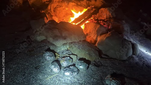 A bonfire on the beach, baked potatoes in foil on the sand and barbecue grilled on coals. Camping photo