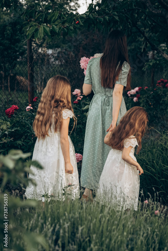 maternal care, care for the younger generation. rear view Mother and daughters in a flower garden
