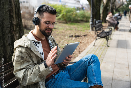 Young freelance hipster generation Z man sitting in park relaxing read emails checking business economy statistics with employee on video call. Smiling businessperson small company owner on vacation